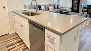 A modern kitchen with white cabinetry, a built-in dishwasher, and a large island with a sink. - Modern Beach Home with Golf Cart! Dog Friendly! (Carolina Beach)