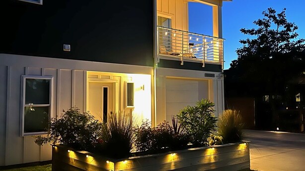 A two-story house with a balcony, a well-lit entrance, and a landscaped front yard. - Modern Beach Home with Golf Cart! Dog Friendly! (Carolina Beach)