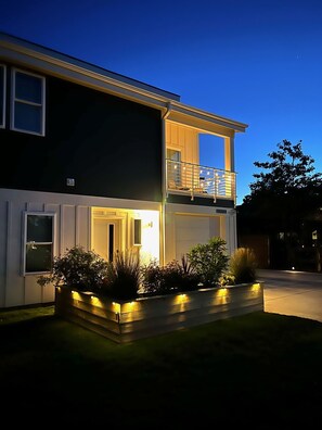 A two-story house with a balcony, a well-lit entrance, and a landscaped front yard. - Modern Beach Home with Golf Cart! Dog Friendly! (Carolina Beach)