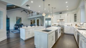 A spacious kitchen with white cabinetry, a large island, and modern pendant lighting. - Tern Key - Luxury Canal-Front Home w/ Heated Pool, Spa, Dock & Near Bean Point (Anna Maria)