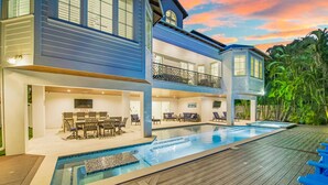 A two-story house with a swimming pool, outdoor furniture, and a 'No Wake' sign. - Tern Key - Luxury Canal-Front Home w/ Heated Pool, Spa, Dock & Near Bean Point (Anna Maria)