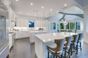 Une cuisine spacieuse avec des meubles blancs, un grand îlot central et des luminaires suspendus.
