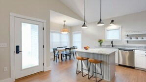 A modern kitchen with a central island, bar stools, pendant lighting, and a dishwasher. - The Cove at Sylvan Beach - Pet friendly lakeside cottage with a pontoon boat! (Sylvan Beach)