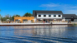 A waterfront property with a large building, a wooden deck, and a dock extending into the water. - The Cove at Sylvan Beach - Pet friendly lakeside cottage with a pontoon boat! (Sylvan Beach)