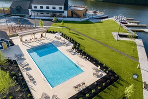 A swimming pool with lounge chairs and a grassy area with a dock and boats.