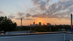 A rooftop terrace with a city skyline at sunset, including a prominent tower and high-rise buildings. - Modern Home With Rooftop Patio - Down Town Views (San Antonio)