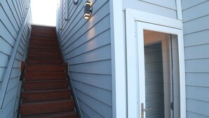 A wooden staircase leading to a door with a glass panel, flanked by light-colored siding walls. - Modern Home With Rooftop Patio - Down Town Views (San Antonio)