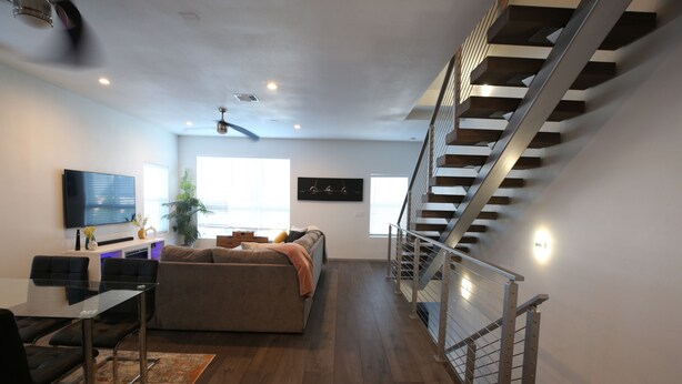 A modern living room with a sofa, a glass dining table, and a staircase. - Modern Home With Rooftop Patio - Down Town Views (San Antonio)