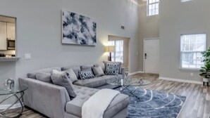 A spacious living room with a grey sectional sofa, a blue patterned rug, and a large abstract painting on the wall. - *Modern oasis 7 mins from Atlanta airport (College Park)