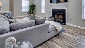 A living room with a large gray sofa, a flat-screen TV mounted above a fireplace, and a wooden floor. - *Modern oasis 7 mins from Atlanta airport (College Park)