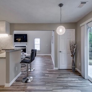 A modern kitchen with a flat-screen TV, a dining area with two chairs, and a hallway with a patterned floor.