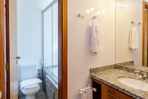A bathroom with a toilet, a sink, and a mirror. There are towels hanging on hooks. - LOCAR-IN GRAMADO-Alphaville (Gramado)