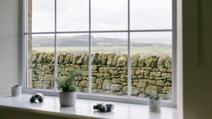 A window with a view of a stone wall and a rural landscape.
