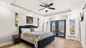 Une chambre dotée d’un grand lit, d’un ventilateur de plafond et offrant une vue sur l’extérieur grâce à une porte-fenêtre coulissante.