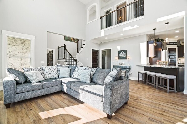 A spacious living area with a grey sectional sofa, a wooden floor, and a staircase leading to an upper level.