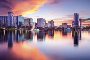 A city skyline with modern high-rise buildings, a body of water reflecting the buildings, and a fountain in the foreground. - 8523 Emerald Island (Kissimmee)