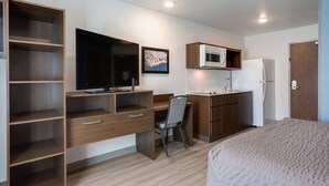 A compact room with a bed, a desk with a chair, a television, a microwave, and a refrigerator.