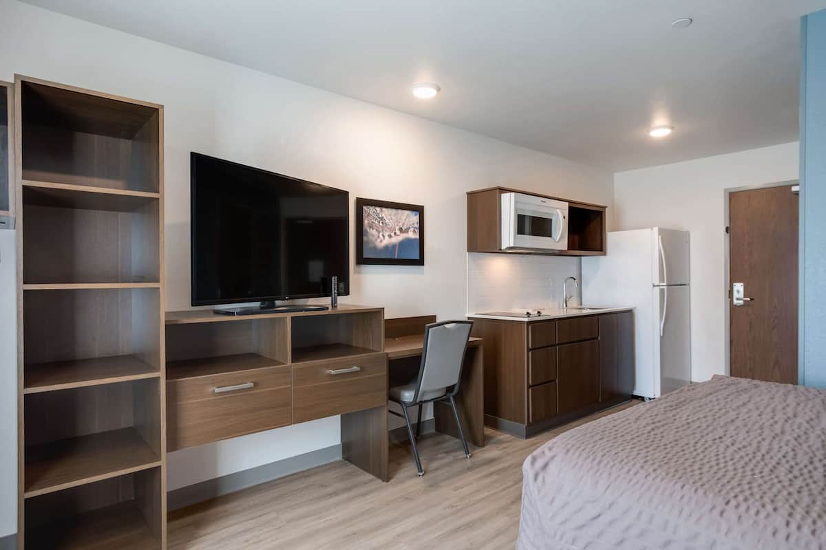 Een compacte kamer met een bed, een bureau met stoel, een televisie, een magnetron en een koelkast.