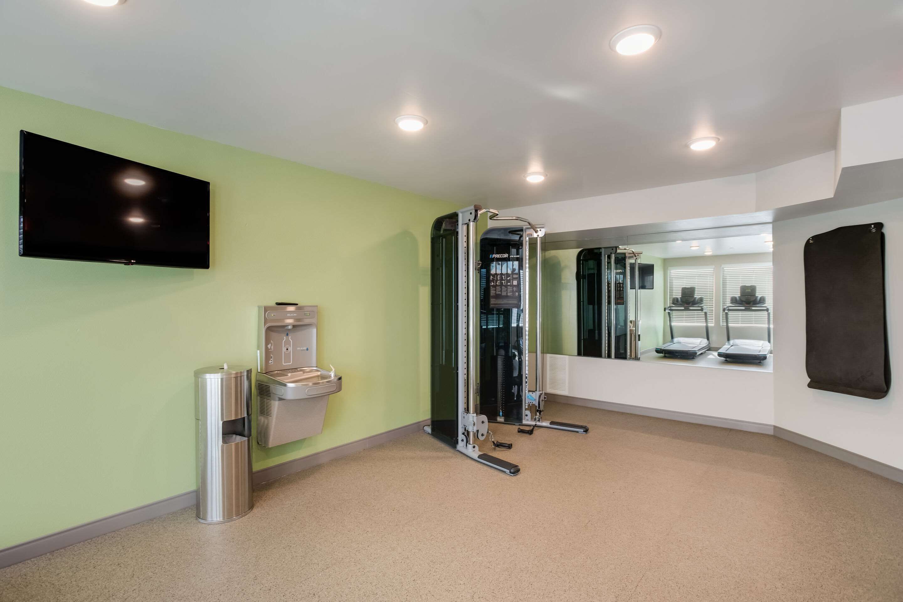 Un gimnasio con barra de dominadas, dispensador de agua, espejo y televisión en la pared.