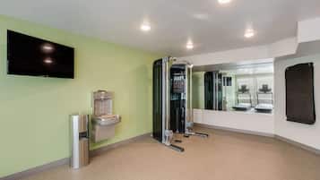 Un gimnasio con barra de dominadas, dispensador de agua, espejo y televisión en la pared.
