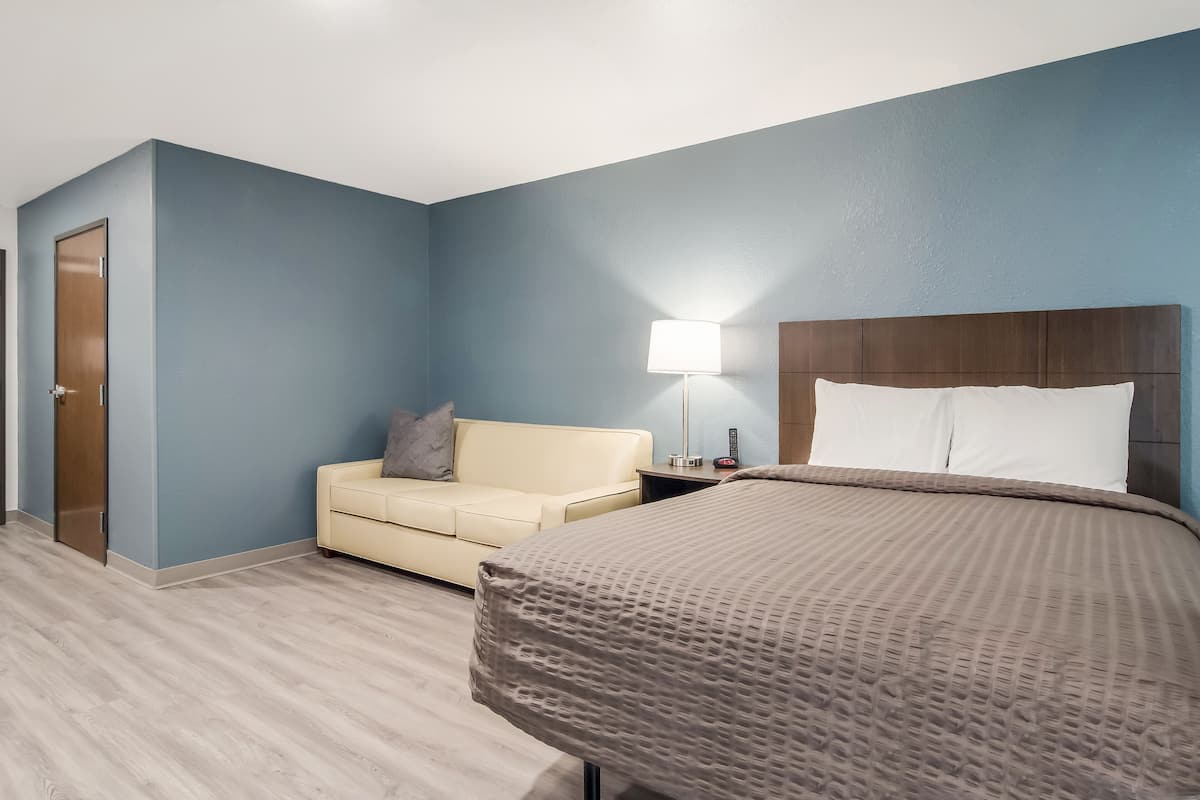 Een hotelkamer met een bed, nachtkastje, lamp, bank en een deur.