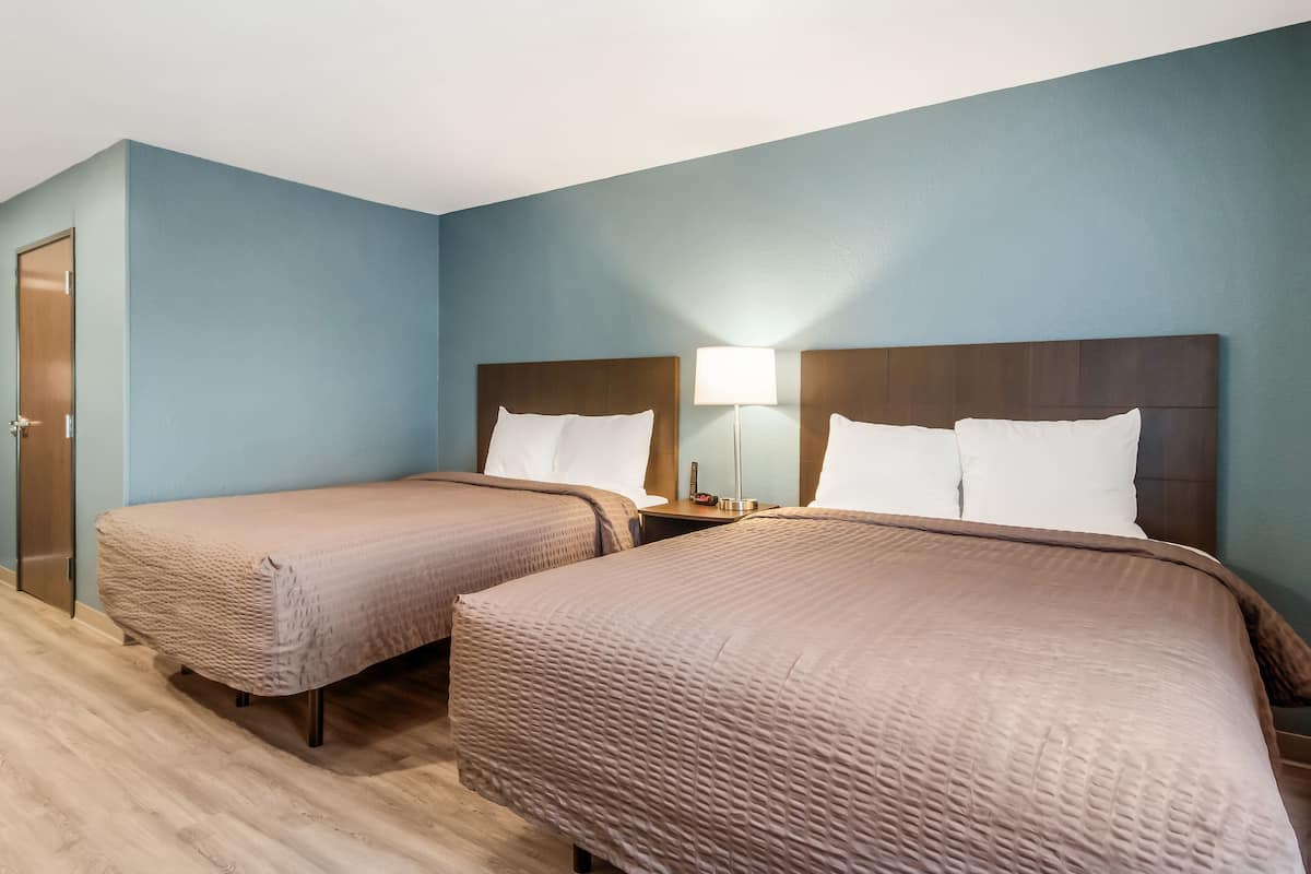 Een hotelkamer met twee eenpersoonsbedden, een houten deur en een nachtkastje met een lamp.