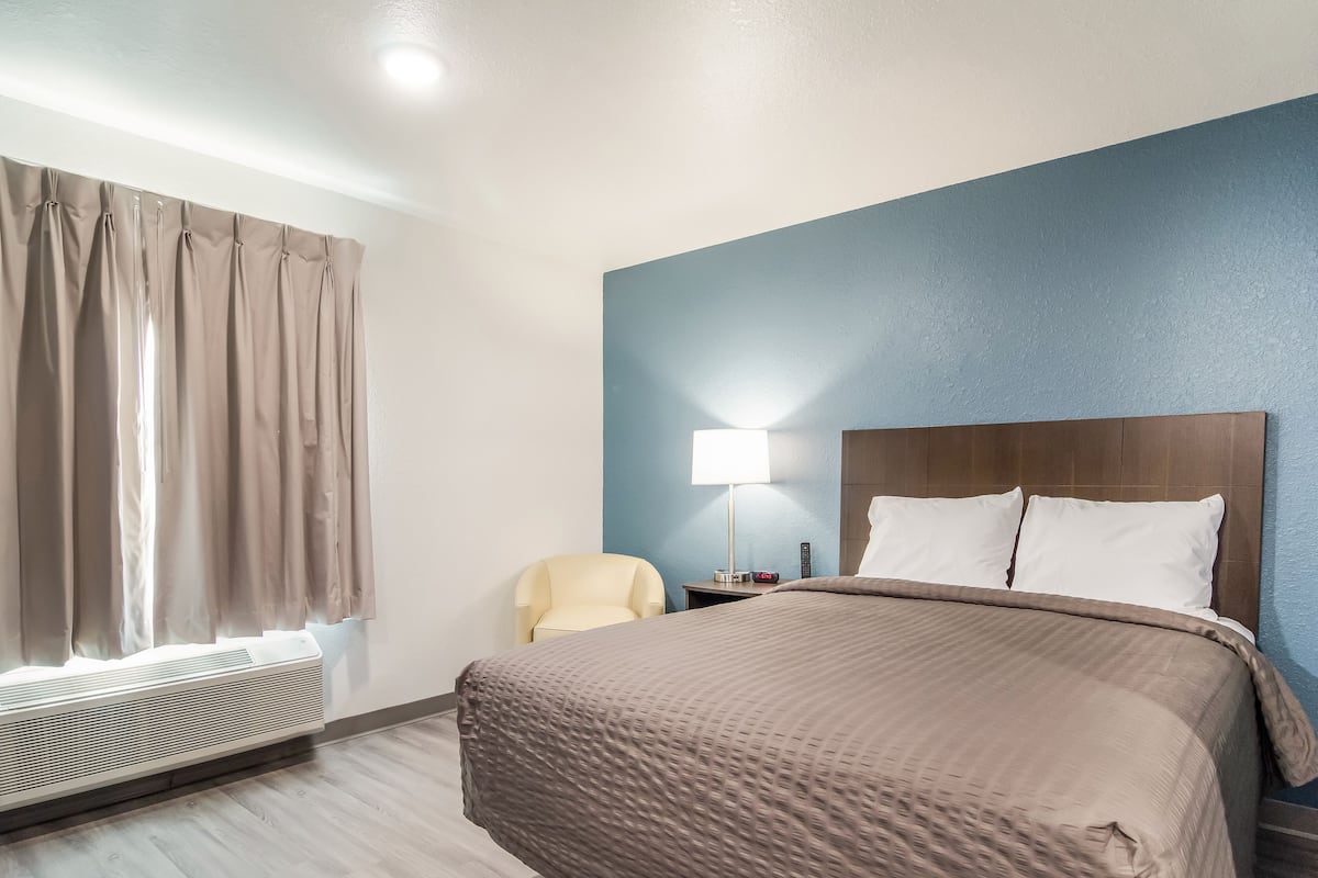 Hotelkamer met een bed, een stoel, een nachtkastje, een lamp en een airconditioning.