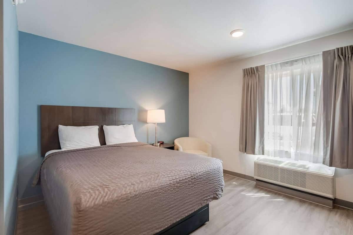 Een hotelkamer met een bed, een stoel, een lamp, een raam met gordijnen en een radiator.