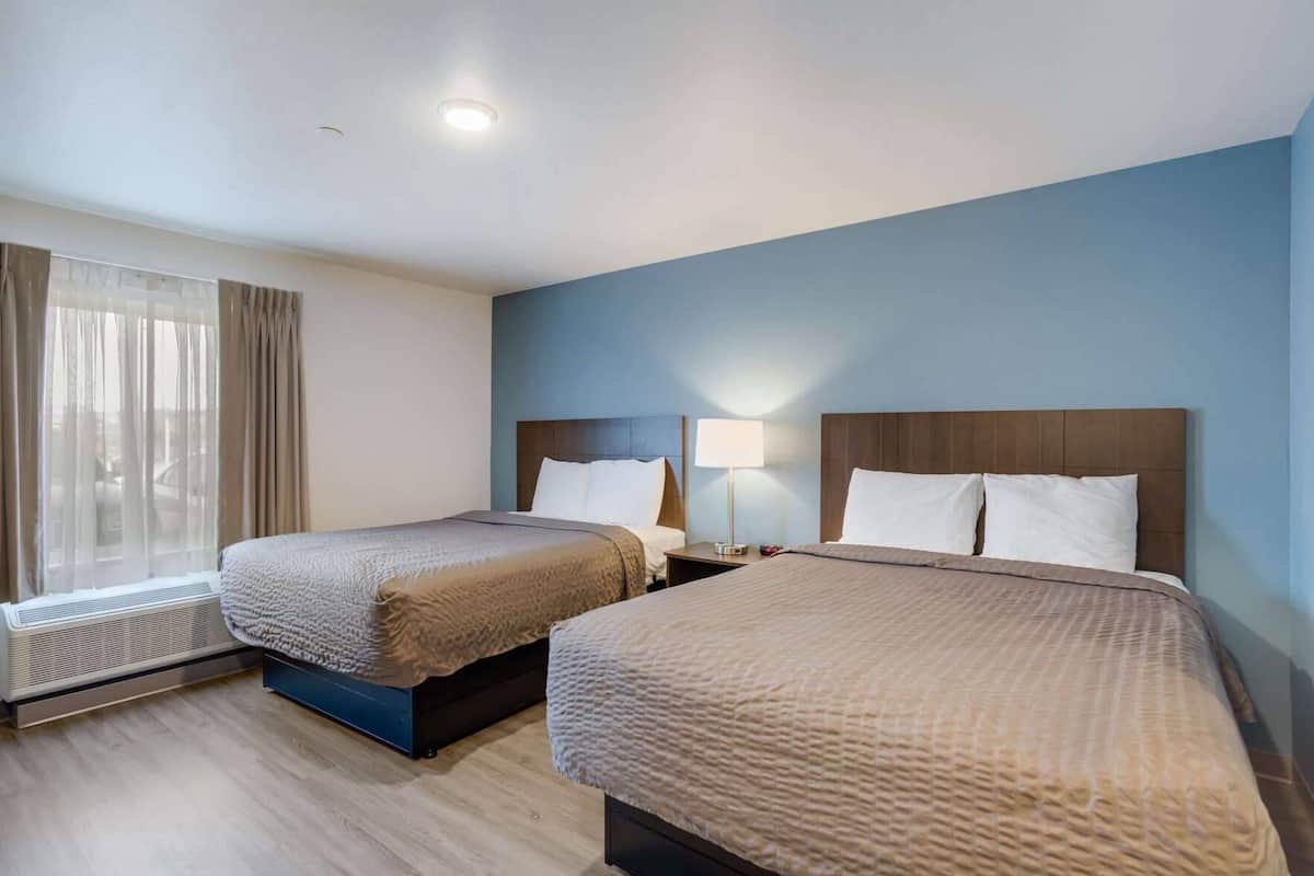 Hotelkamer met twee bedden, een raam met gordijnen, een nachtkastje met een lamp en een wandradiator.