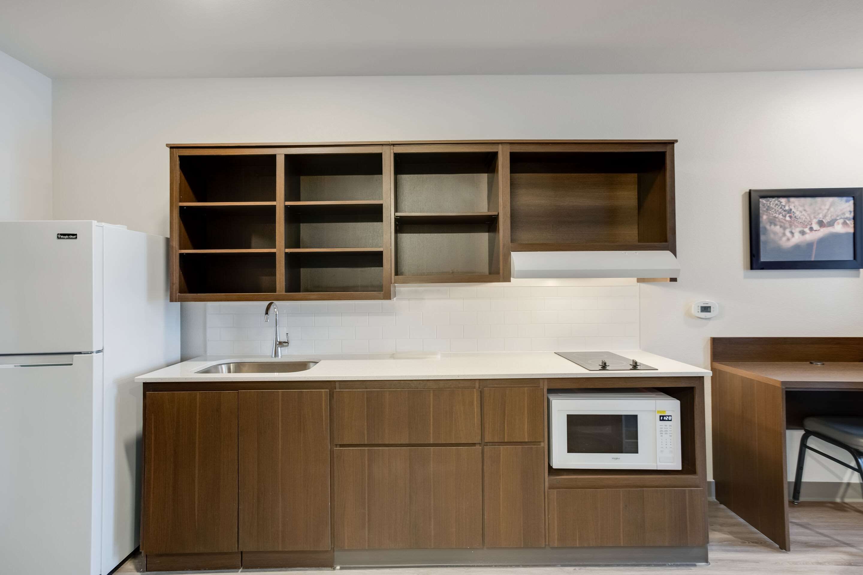 Una cocina compacta con armarios de madera, microondas integrado y un refrigerador blanco.