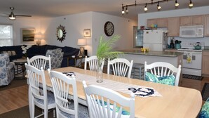 A dining area with a wooden table and white chairs, a kitchen with wooden cabinets and modern appliances, and a living room with a sofa and decorative pillows.