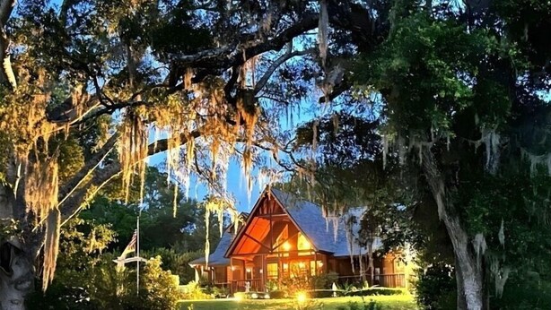 A rustic cabin with a triangular roof, surrounded by trees and a well-maintained lawn. - Cabin On The Lake (Lake Helen)