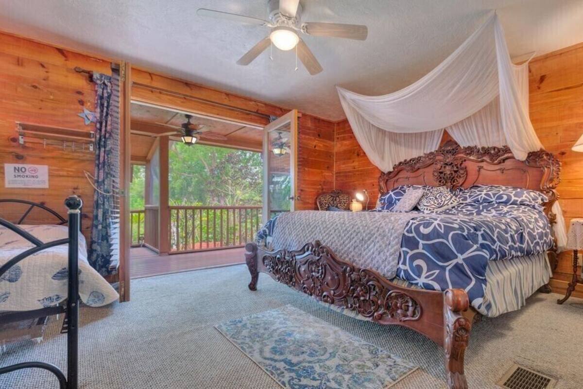 Een slaapkamer in een houten hut met een groot bed, een plafondventilator en een balkon met een 'Niet roken'-bord.