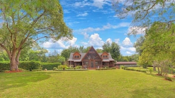 Stately two-story house with a gabled roof and large front porch, set amidst well-mainters lawns and mature trees.
