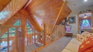 A wooden interior with a sloped ceiling, a staircase, a chair with a Union Jack flag, and a window with curtains. - Cabin On The Lake (Lake Helen)