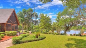 A lodge with a triangular roof and large windows, surrounded by a well-maintained lawn and trees. - Cabin On The Lake (Lake Helen)