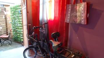 Uma bicicleta estacionada num quarto com cortina vermelha e uma bolsa presa à parede.