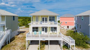 A two-story beachfront property with a balcony, a covered entryway, and a visible trash receptacle.