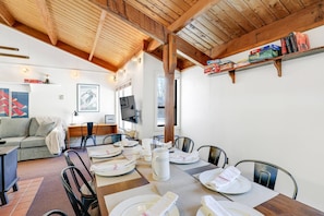Un comedor con una mesa de madera dispuesta para cuatro personas, un sofá y un televisor sobre un mueble.