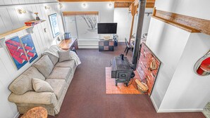A cozy living room with a sofa, a TV, a fireplace, and a rustic wooden ceiling. - Happy Haven (Thornton)
