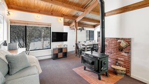 A cozy living room with a fireplace, wooden beams, a TV, and a dining area. - Happy Haven (Thornton)