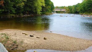 A river with a wooden bridge and a sandy bank with rocks. - Happy Haven (Thornton)