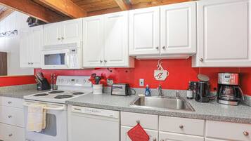 A kitchen with white cabinets, a red backsplash, a stove, a microwave, a dishwasher, and a coffee maker.