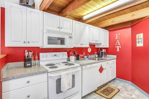 Una cocina con armarios blancos, un microondas, una estufa y una pared roja con la palabra "EAT" escrita.