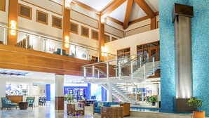 Eine geräumige Lobby mit hoher Decke, Holzbalken, einer zentralen Treppe und Sitzbereichen.