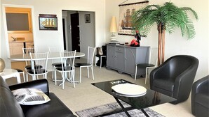 Ein modernes Wohnzimmer mit einem schwarzen Ledersofa, weißen Stühlen, einem Glastisch und einem Essbereich mit weißem Tisch und Stühlen.