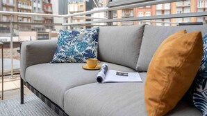Een moderne woonkamer met een grijze bank, een gele kop en een opgerold tijdschrift op een vensterbank.
