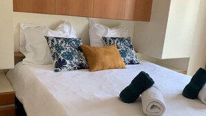 Een net opgemaakt bed met wit beddengoed, twee kussens met een bladmotief, en een bruin accentkussen.