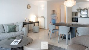 Een moderne woonkamer met een bank, salontafel en eethoek. Een bordje geeft aan: “Verdieping 1, Seaside”.