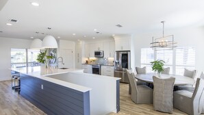 Una cocina moderna con una isla central, muebles blancos y un comedor con sillas tapizadas en gris.